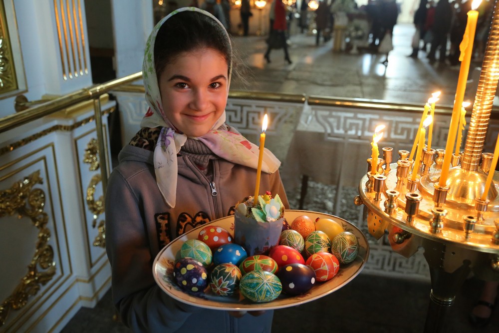Девочка в церкви с куличом и крашеными яйцами в руках
